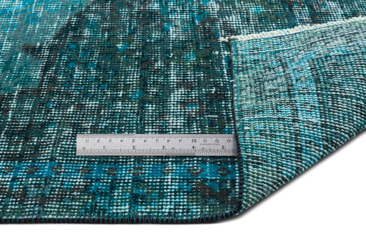 Teal and dark blue distressed rug with a faded traditional pattern, shown with a metal ruler for scale.