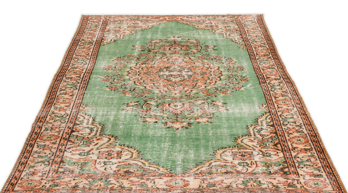 Distressed green rug with a central orange and cream floral medallion and ornate geometric border.