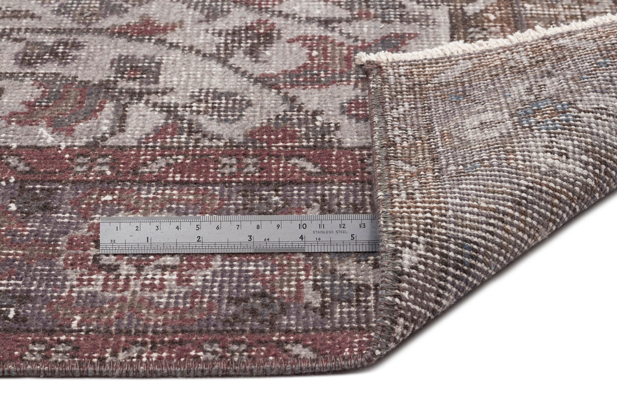 Distressed grey and burgundy floral medallion rug with a folded corner and a metal ruler for scale.
