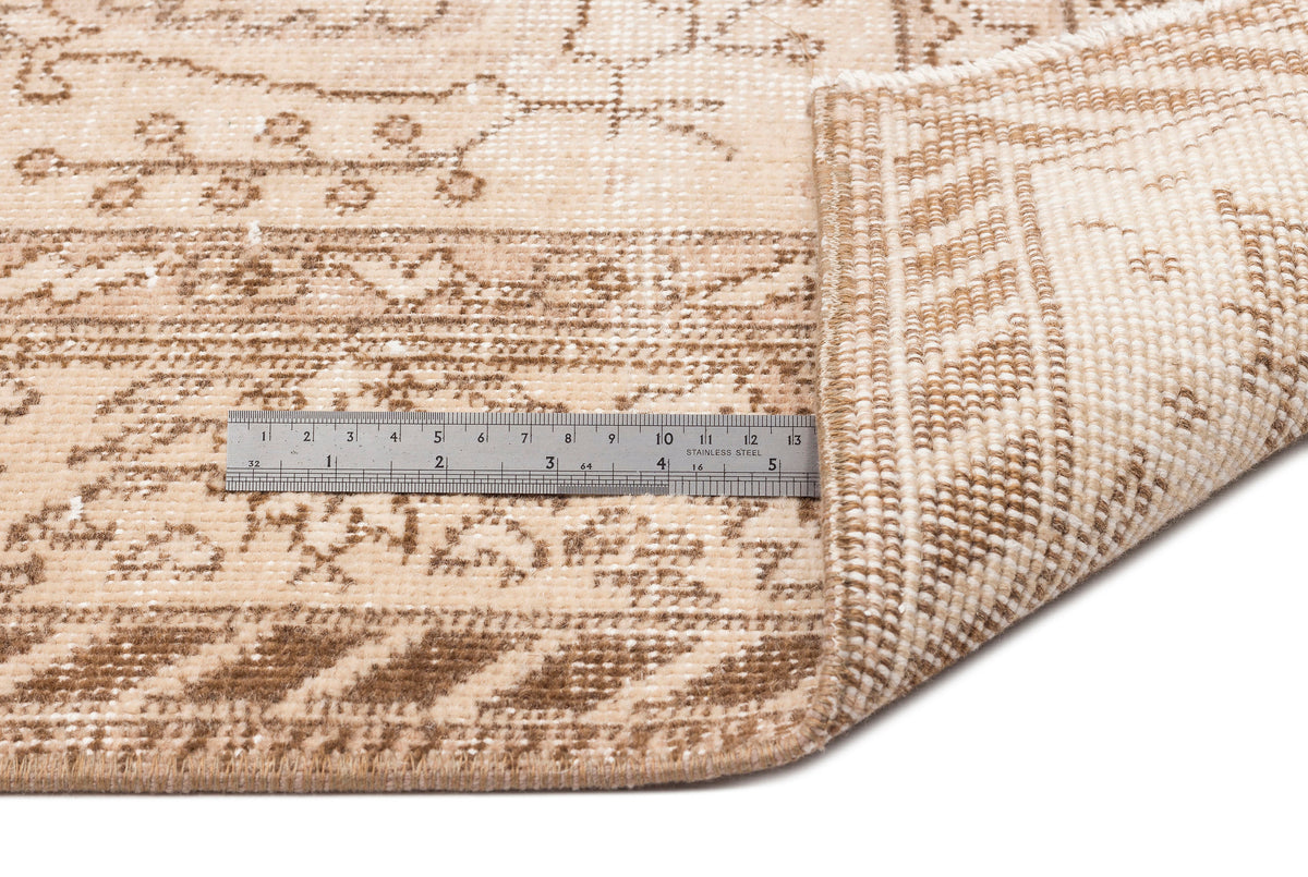 Beige and brown distressed traditional rug with a folded corner and a metal ruler for scale.