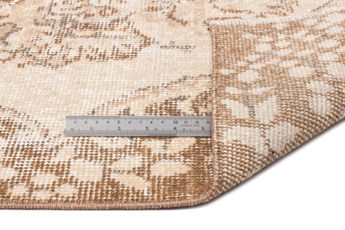 Load image 1 in gallery view. Beige and brown distressed medallion rug with a folded corner and a metal ruler for scale on a white background.