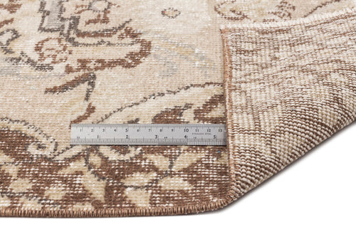 Load image 1 in gallery view. Beige and brown distressed floral rug with a folded corner revealing the woven backing and a metal ruler for scale.