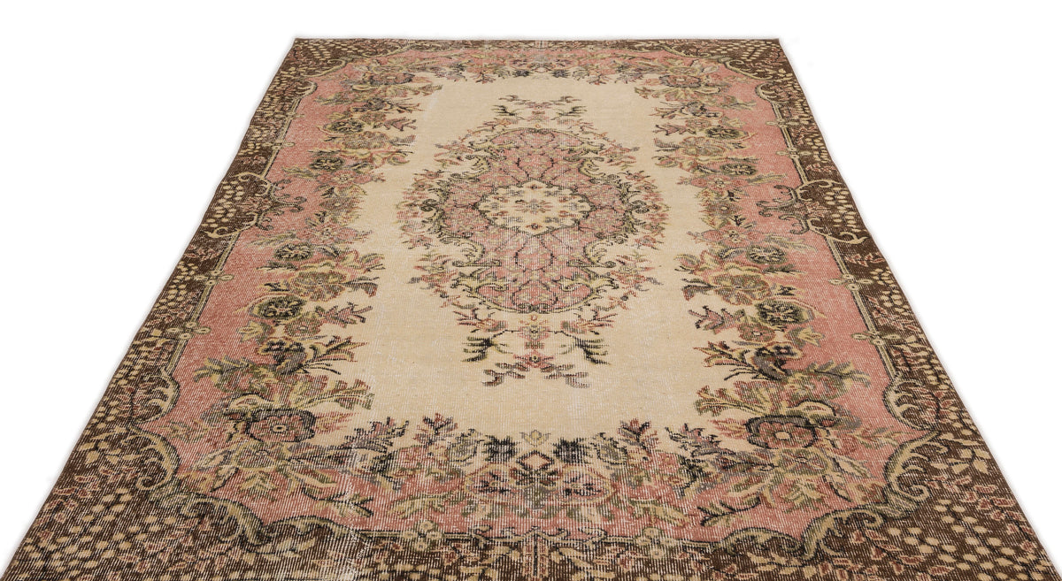 Distressed beige, pink, and brown rug with a central floral medallion and ornate botanical border.