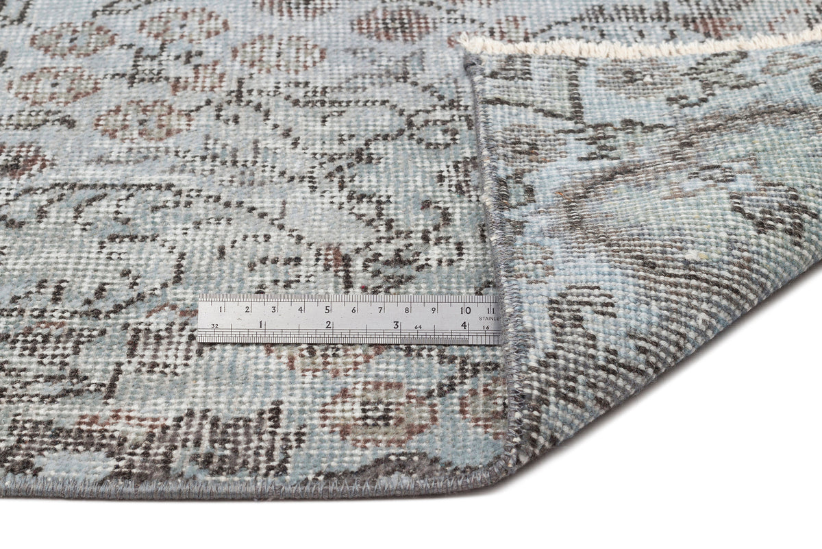 Light blue and grey distressed rug with a traditional floral pattern, shown with a metal ruler for scale.
