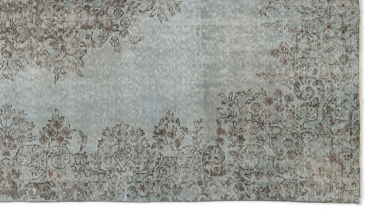 Distressed light blue rug with a faded brown floral pattern and a fringed edge.