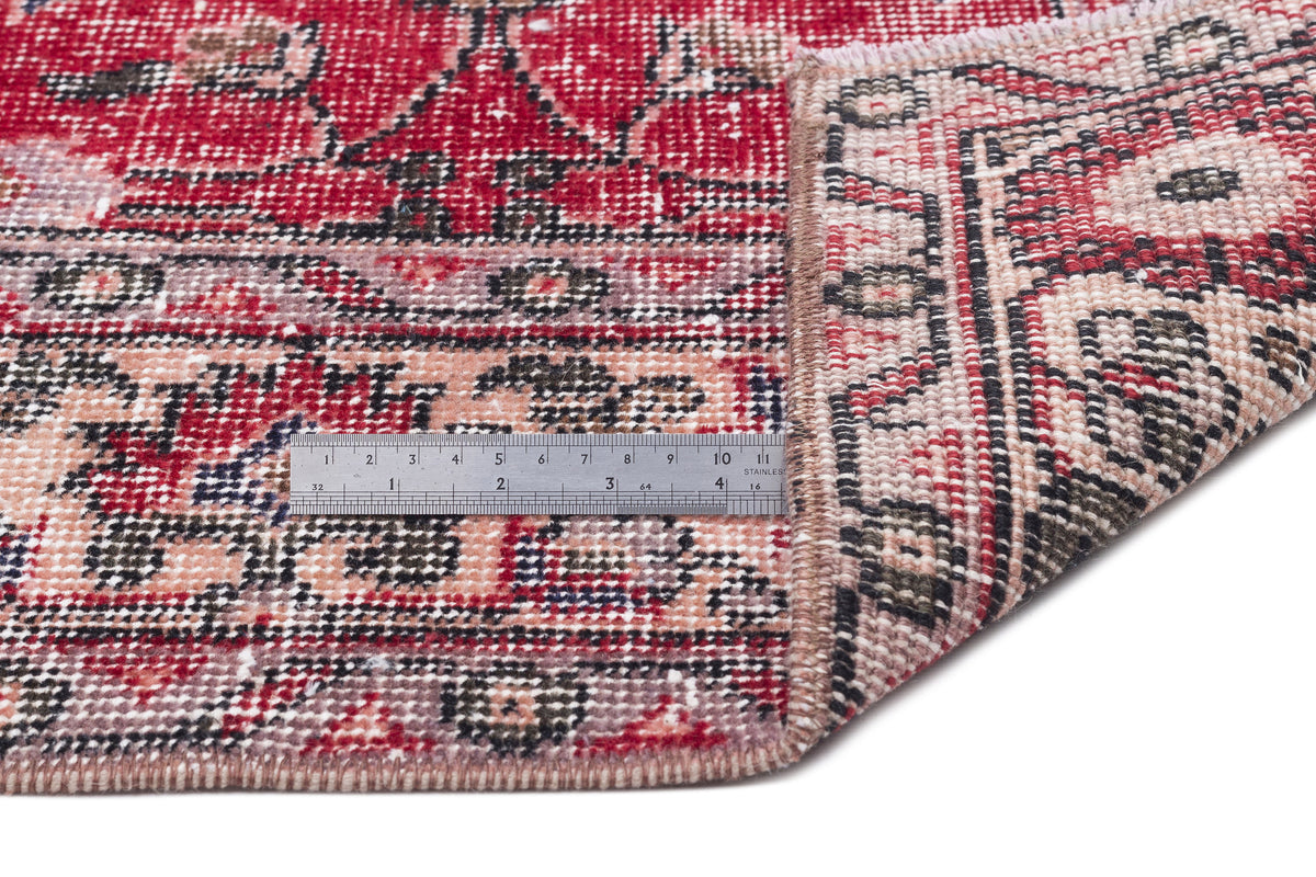 Red and beige vintage-style rug with a distressed floral pattern, shown with a metal ruler for scale.