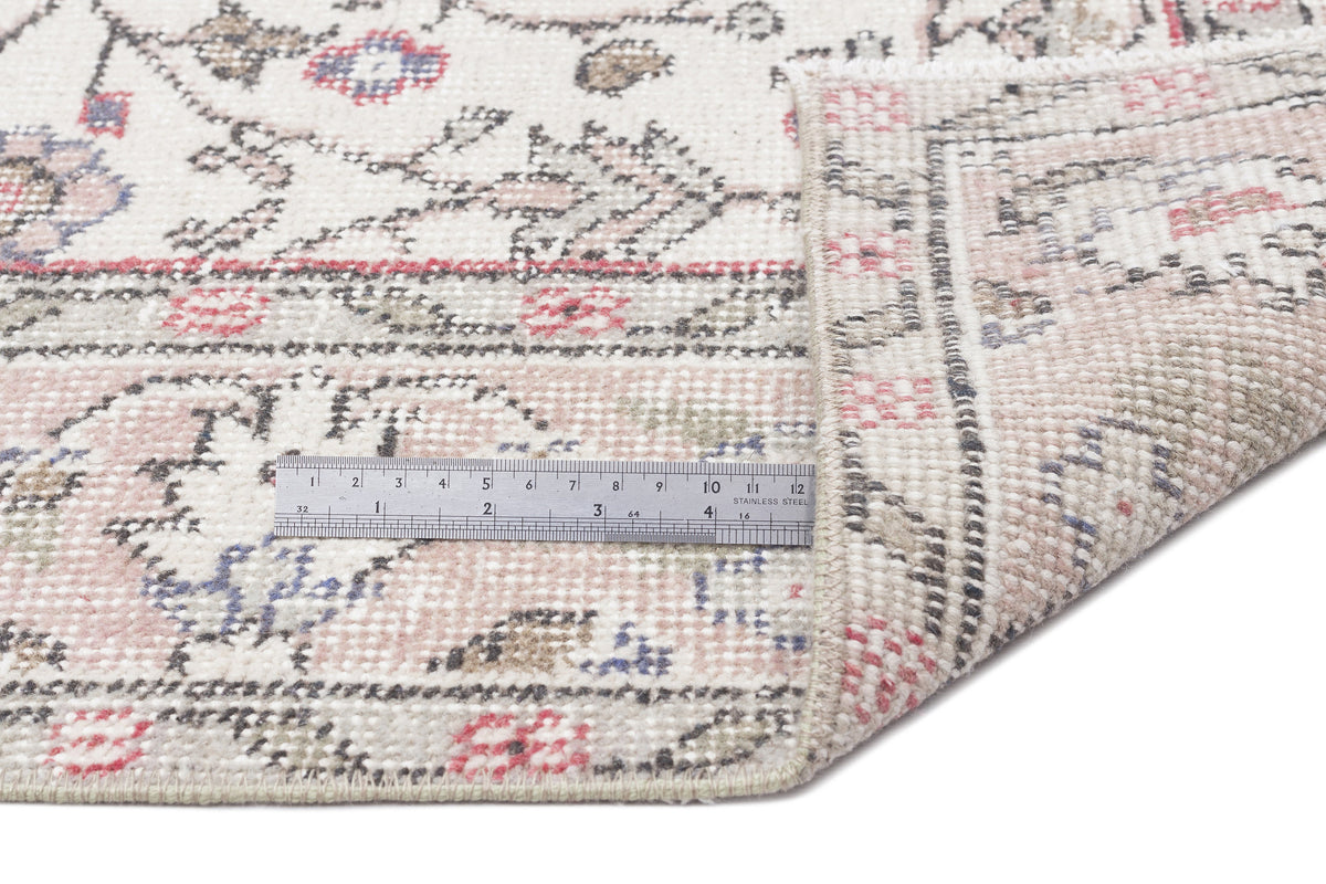 Cream, pink, and grey traditional rug with a floral pattern, shown with a metal ruler for scale on a white background.