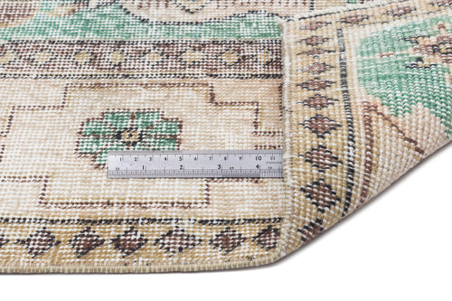 Load image 1 in gallery view. Beige, green, and brown traditional patterned rug with a folded corner and a metal ruler for scale.
