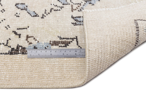Load image 1 in gallery view. Beige rug with a faded blue and brown geometric pattern, shown with a metal ruler for scale on a white background.