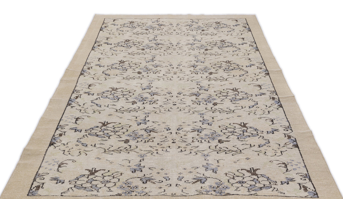Beige area rug with a distressed floral pattern in muted blue and charcoal gray on a white background.