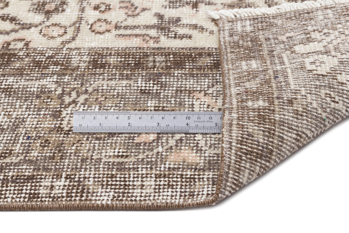 Brown and cream distressed traditional rug with a folded corner and a metal ruler for scale on a white background.