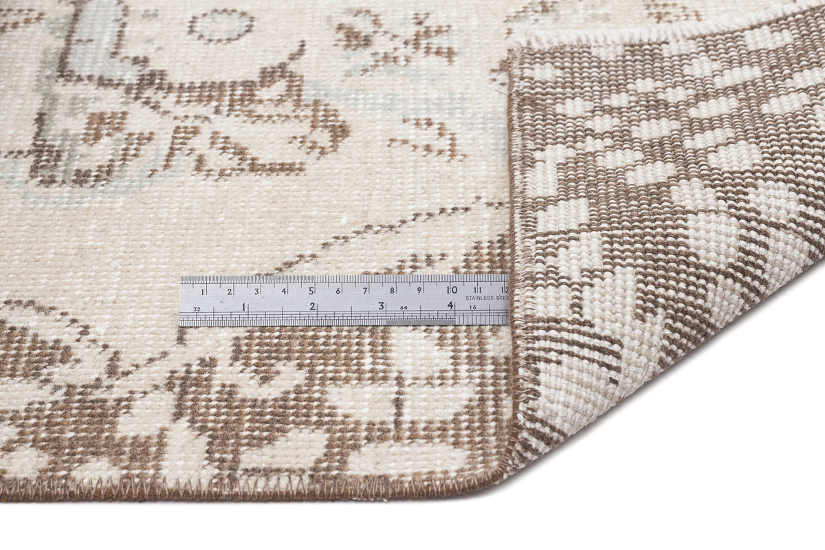 Beige and brown distressed traditional rug with a folded corner and a metal ruler for scale on a white background.