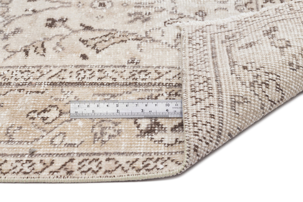 Beige and brown distressed traditional rug with a folded corner and a metal ruler for scale on a white background.