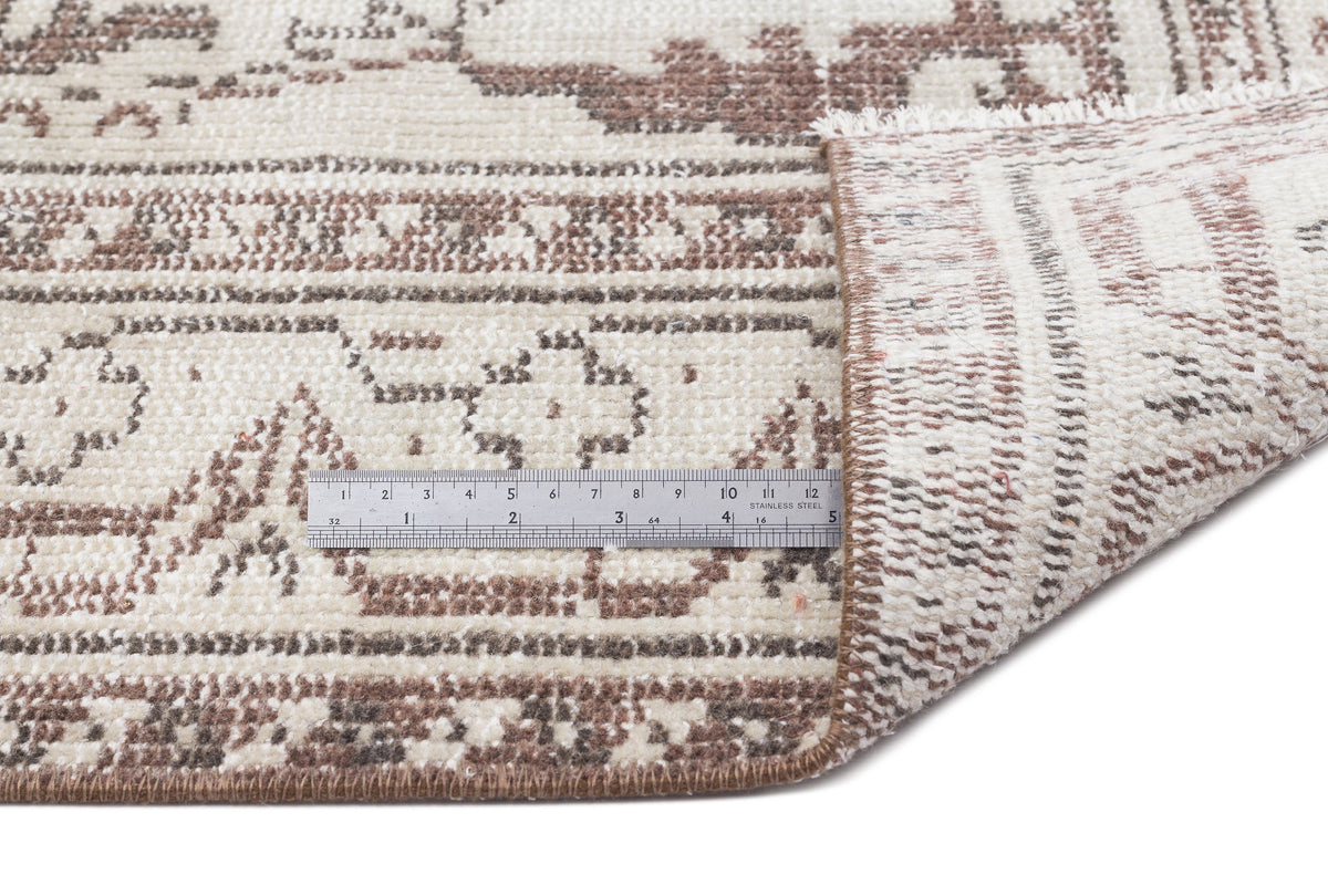 Cream and brown distressed traditional rug with a folded corner and a metal ruler for scale on a white background.