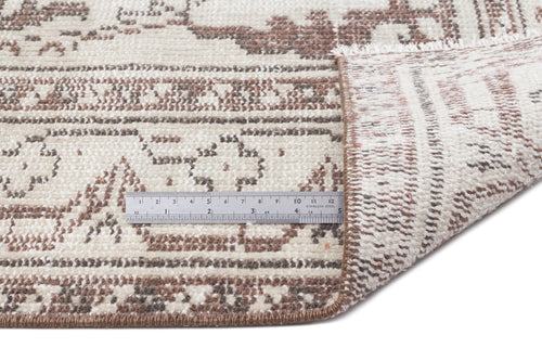 Load image 1 in gallery view. Cream and brown distressed traditional rug with a folded corner and a metal ruler for scale on a white background.