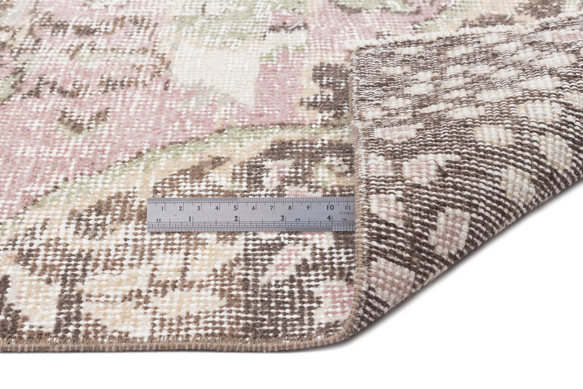 Distressed pink, brown, and cream floral medallion rug with a folded corner and a metal ruler for scale.