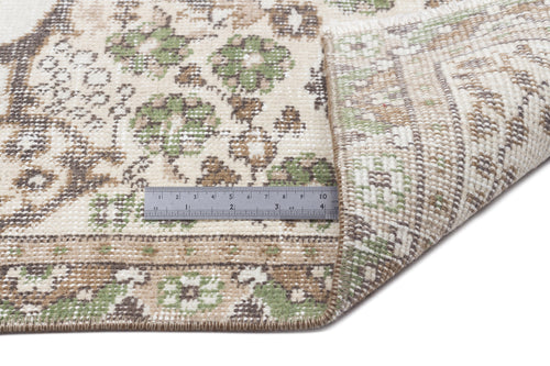 Load image 1 in gallery view. Cream, sage green, and brown floral medallion rug with a corner folded back to show the woven backing and a metal ruler.