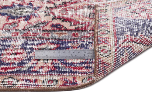 Load image 1 in gallery view. Distressed floral medallion rug in red, blue, and beige with a folded corner and a metal ruler for scale.