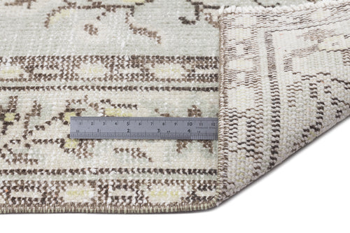Load image 1 in gallery view. Sage green and cream rug with a distressed floral pattern, shown folded to reveal the underside with a metal ruler.