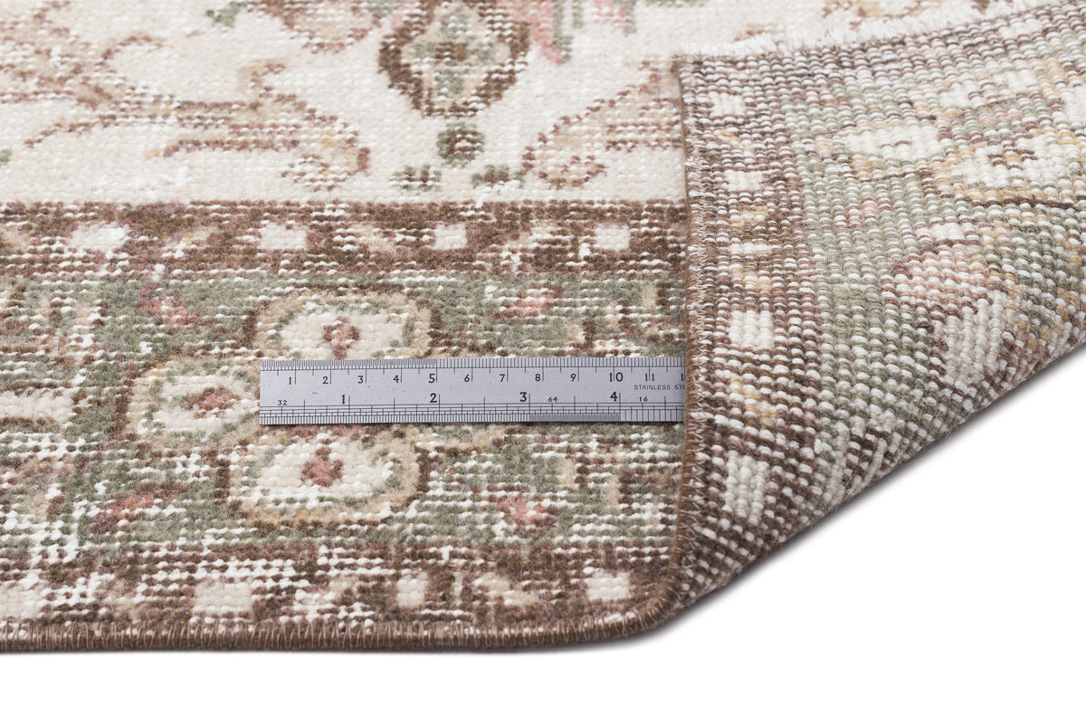Cream, sage green, and brown rug with a distressed floral pattern, shown with a metal ruler for scale.