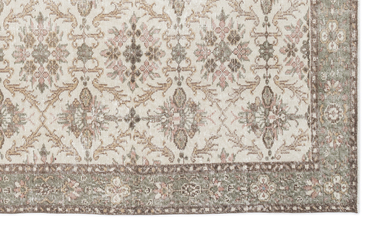 Cream rug with a distressed floral medallion pattern in muted sage, brown, and dusty pink, featuring a wide border.