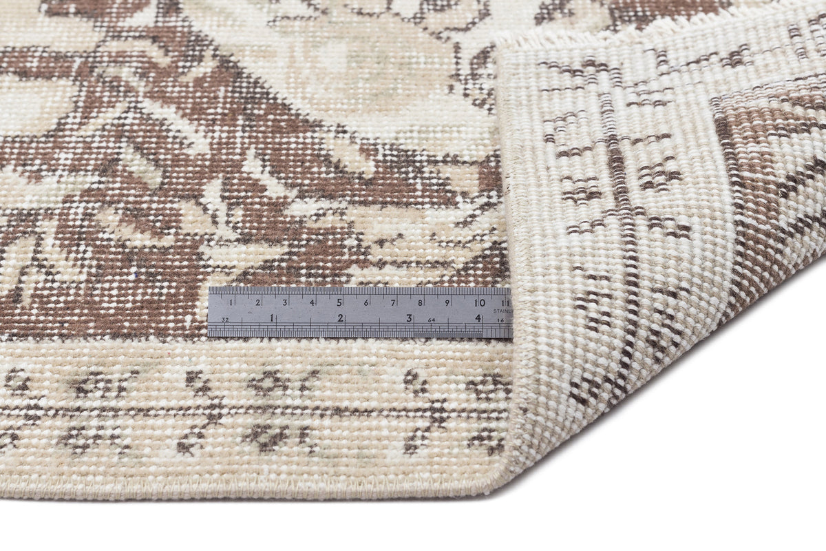 Brown and beige rug with a traditional distressed medallion pattern, shown with a metal ruler for scale.
