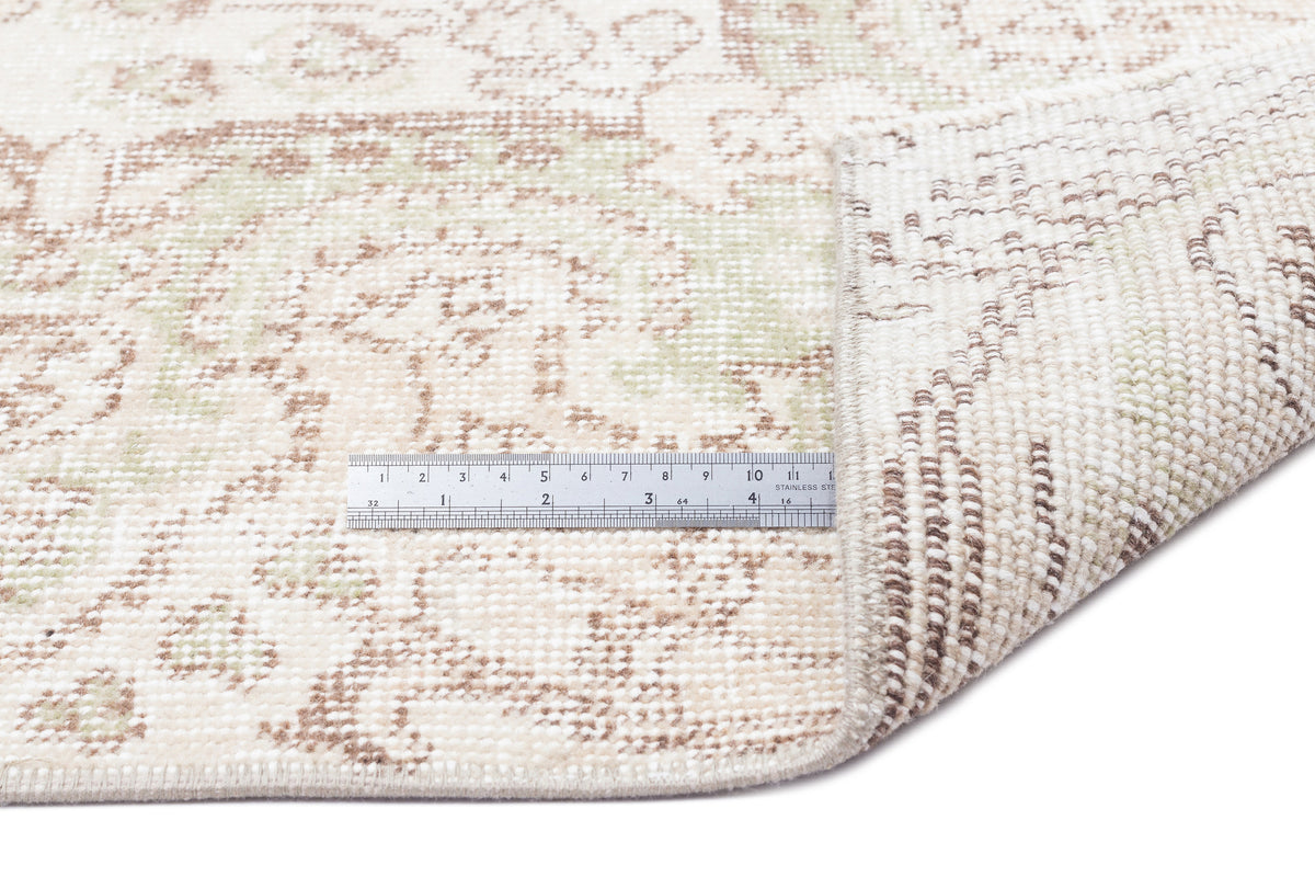 Cream, beige, and sage green rug with a distressed medallion pattern, shown with a metal ruler for scale.