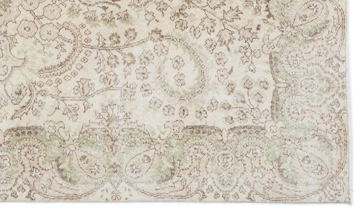 Cream rug with a distressed, faded floral medallion pattern in sage green and brown tones.