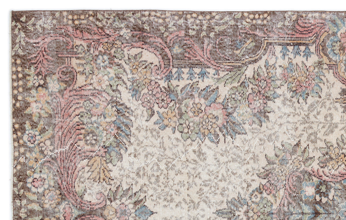 Distressed vintage-style rug with a brown, cream, pink, and blue floral medallion pattern.
