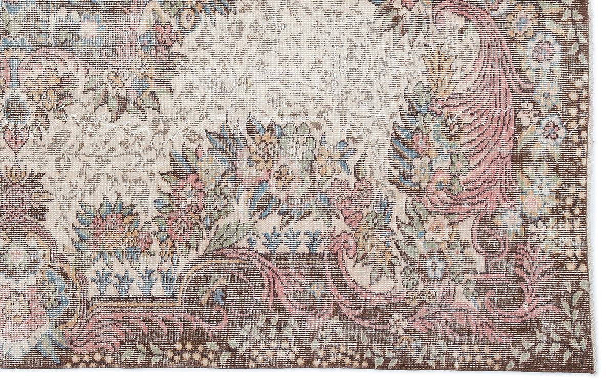 Distressed traditional rug with a cream field, brown border, and floral motifs in muted pink, blue, and green.