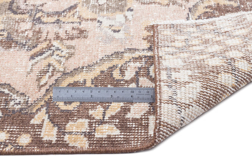 Load image 1 in gallery view. Distressed beige and brown floral medallion rug with a folded corner and a metal ruler for scale on a white background.