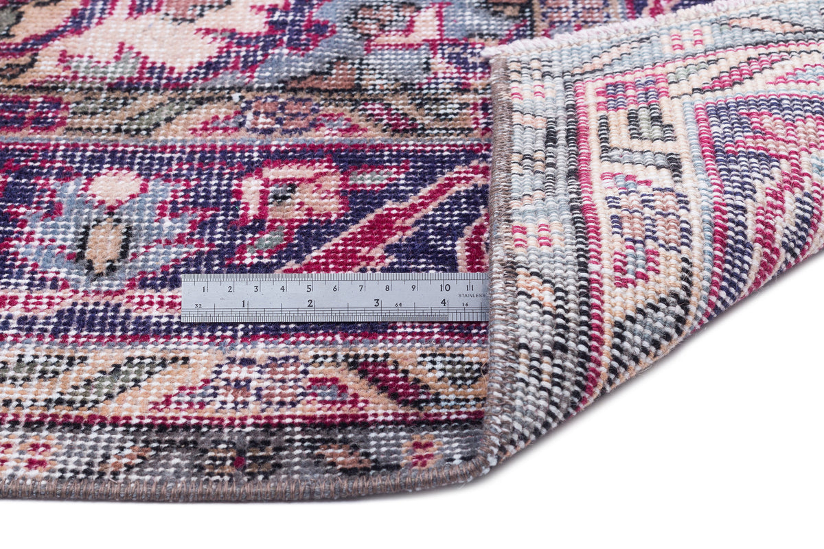 Distressed floral medallion rug in magenta, navy, and cream with a folded corner and a metal ruler for scale.