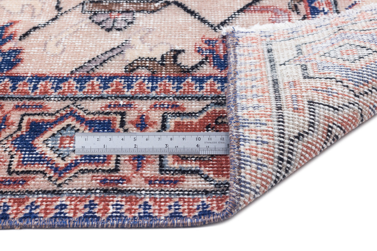 Beige, blue, and terracotta traditional patterned rug with a folded corner and a metal ruler for scale.