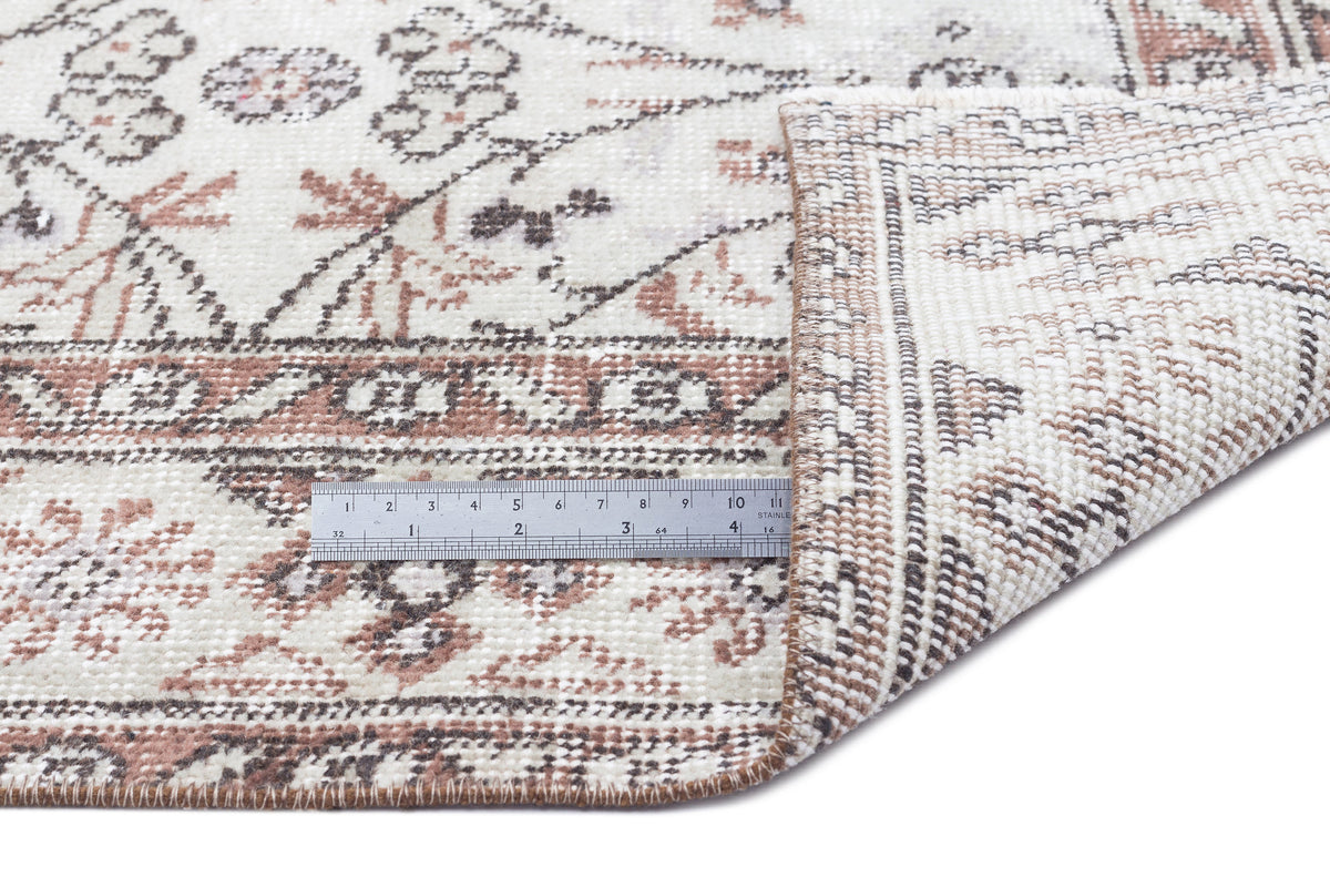 Cream, brown, and terracotta vintage-style rug with a floral medallion pattern, shown folded with a metal ruler.