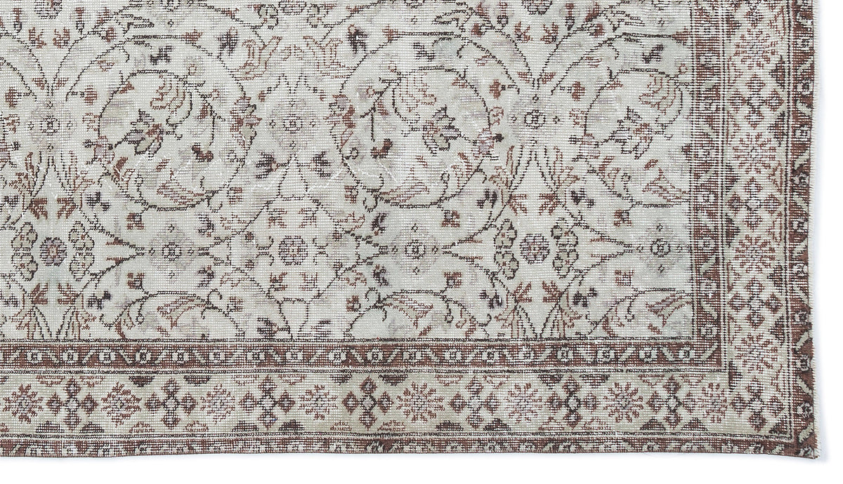 Distressed cream and brown rug with a traditional floral medallion pattern and a geometric border.