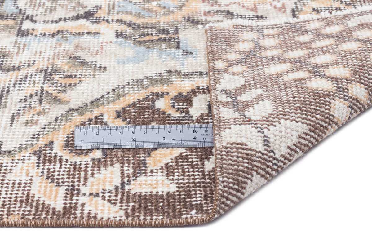 Distressed brown, cream, and blue floral medallion rug with a metal ruler showing scale, isolated on white.