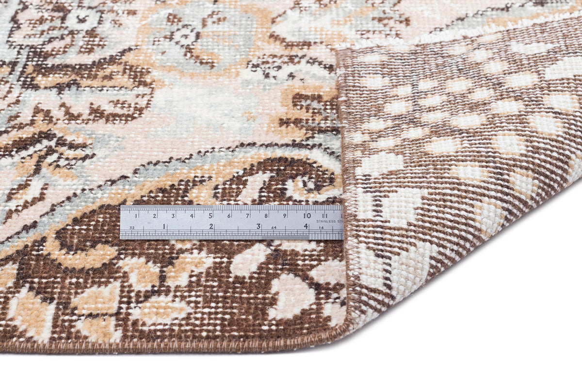 Brown, beige, and light blue distressed floral rug with a folded corner showing the backing and a metal ruler.