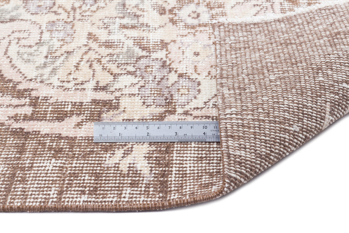 Beige and cream distressed floral rug with a folded corner revealing the woven backing and a metal ruler for scale.