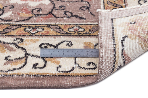 Load image 1 in gallery view. Brown and cream traditional rug with a floral border and a metal ruler showing pile height, isolated on white.
