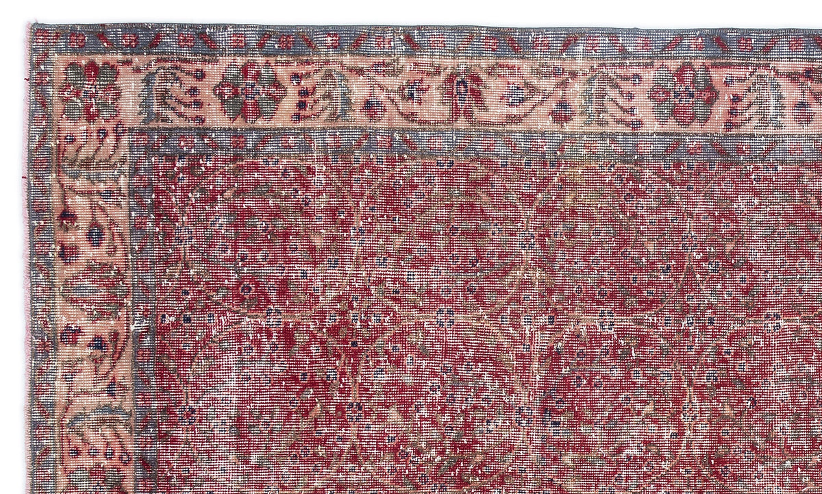 Distressed red rug with a faded floral border and a repeating geometric medallion pattern in blue and cream.