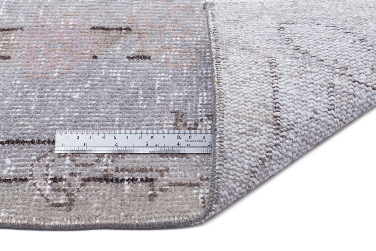 Grey and beige distressed rug with a faded traditional pattern, shown with a metal ruler for scale on a white background.