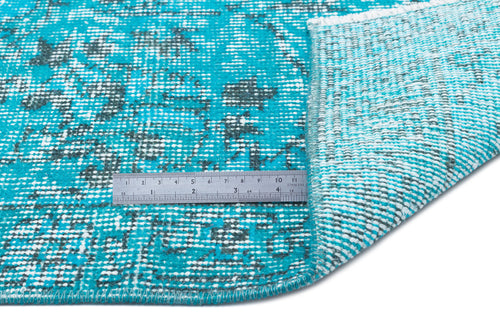 Load image 1 in gallery view. Turquoise and charcoal distressed floral rug with a folded corner and a metal ruler for scale on a white background.