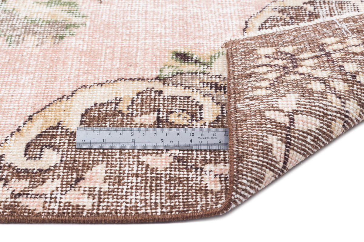 Pink and brown floral medallion rug with a folded corner and a stainless steel ruler for scale.