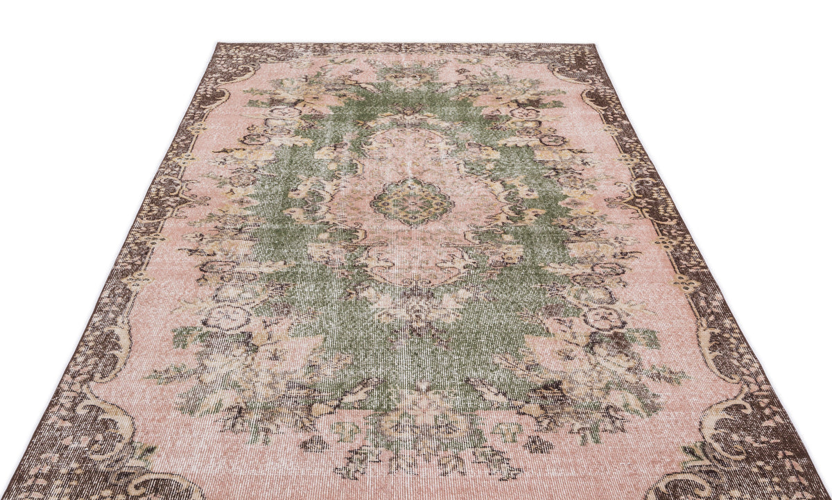 Distressed pink and green vintage-style rug with a central floral medallion and dark brown ornate border.