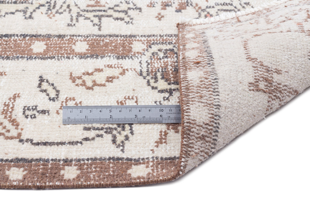 Cream and brown distressed traditional rug with a folded corner and a metal ruler for scale on a white background.