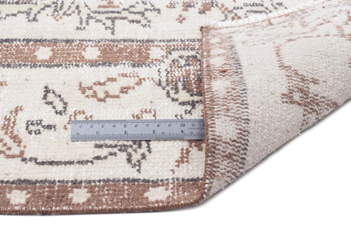Load image 1 in gallery view. Cream and brown distressed traditional rug with a folded corner and a metal ruler for scale on a white background.