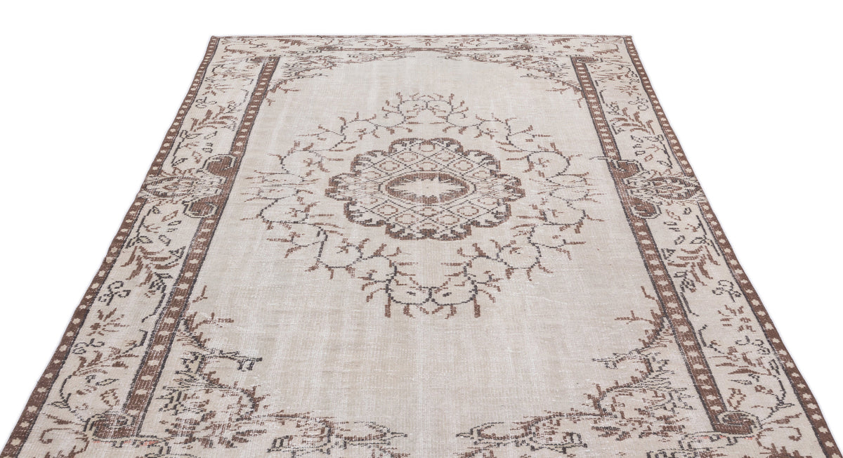 Beige and brown distressed rug with a central floral medallion and geometric border pattern on a white background.