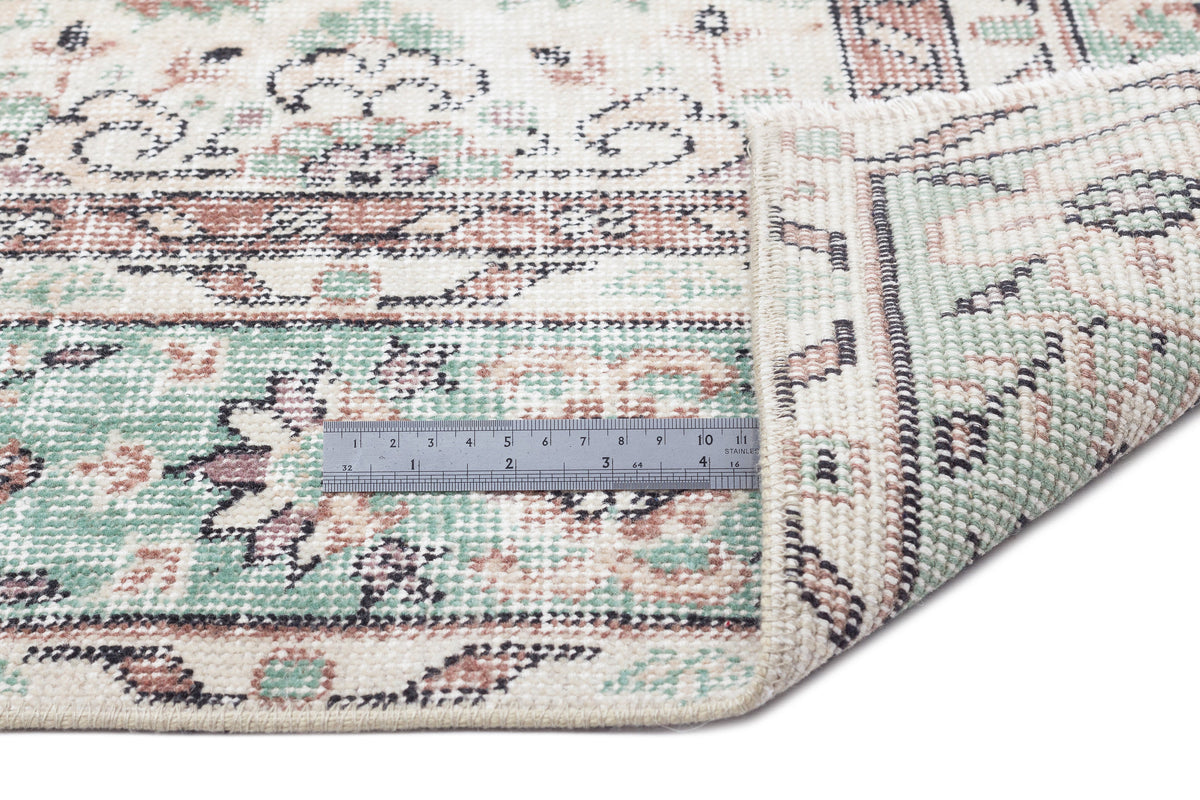 Cream, sage green, and terracotta distressed traditional rug with a folded corner and a metal ruler for scale.