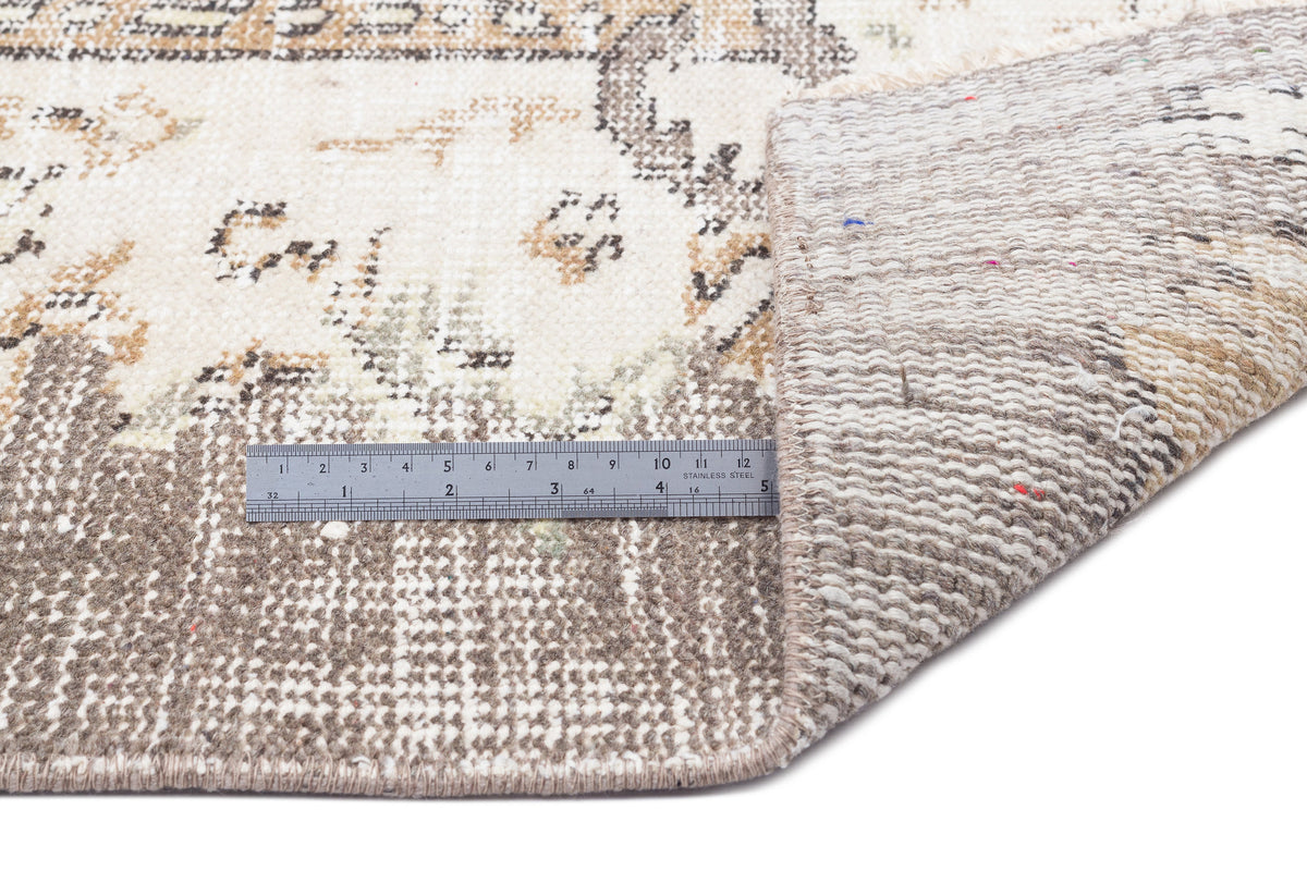 Beige and cream distressed rug with a faded traditional pattern, shown with a metal ruler for scale.