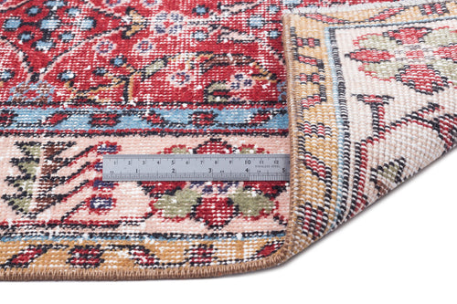 Load image 1 in gallery view. Red, pink, and blue traditional floral rug with a folded corner and a metal ruler for scale on a white background.